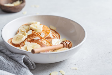 Traditional pancakes with banana, almonds and honey in white plate.