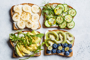 Breakfast toasts with various healthy toppings. Sandwiches  with cream cheese, fruits, berries and honey, salted toasts with avocado and cucumber, top view.