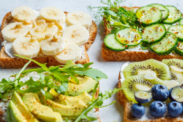 Breakfast toasts with various healthy toppings. Whole grain toasts with cream cheese, fruits, berries and honey, salted toasts with avocado and cucumber.