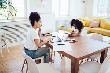 Fototapeta premium Freelance young woman having phone call sitting with small daughter at home