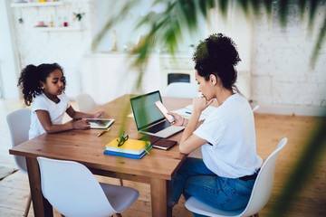 Fototapeta premium Black mother using smartphone and daughter playing on tablet