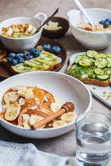 Healthy vegan breakfast table. Oatmeal with fruits, chia pudding, pancakes with banana and honey and toasts with fruits, vegetables and cream cheese.