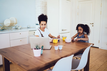 Mother surfing laptop near daughter in morning