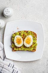 Breakfast avocado toast with egg on a white plate.