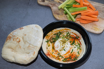 Hummus with tahini, paprika, cumin and parsley, served with pita bread and veggie sticks. Close up view.
