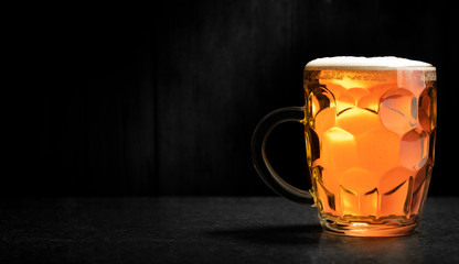 Beer in a mug. A light beer with foam in a mug, a beautifully lit stage with a black top and a black background. Space for an inscription, logo or recipe.
