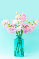 Bouquet of soft pink sweet peas Lathyrus in beautiful transparent vase on blue background.Copy space.Spring concept.Postcard for International Women's Day on March 8, Valentine's Day,14 of February