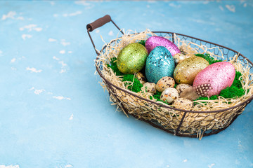 Spring Easter background for spring holidays. Easter composition with colorful Easter eggs on moss in basketon blue table. Top view, copy space