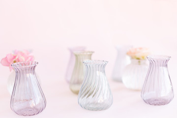 Obraz na płótnie Canvas Small glass crystal vases for decoration of blooming sweet pea Lathyrus, bush roses on pink background. Design, Creative. International Women's Day,March 8 and Valentine's Day,14 of February