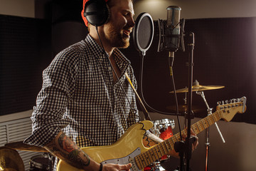awesome caucasian musician play electric guitar and sing in recording studio. man preparing,...