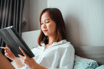 young woman working on tablet computer while sitting at the bedroom. work from home concept