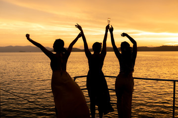 Young women enjoying view of sunset in the ocean while sailing in yacht. One of them hold glass of champaign to celebrate their vacation. Luxury lifestyle concept.