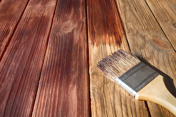 a wooden brush lies on a half painted red stain on the wooden surface top side view