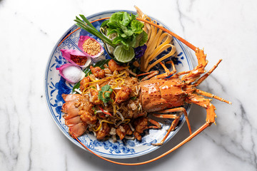 Luxury food presentation of lobster padthai made from whole Phuket lobster and padthai on chineseware on white marble.