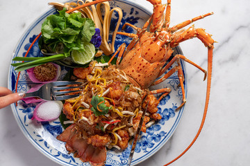 Luxury food presentation of lobster padthai made from whole Phuket lobster and padthai on chineseware on white marble.