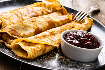 Sweet crepes with fruit jam on wooden table
