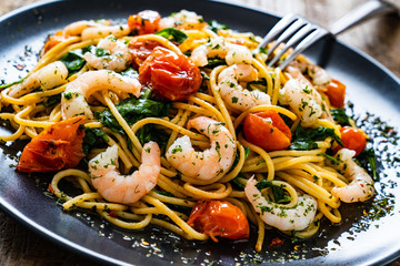 Spaghetti with prawns and vegetables on wooden background