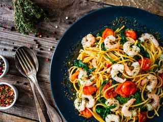 Spaghetti with prawns and vegetables on wooden background