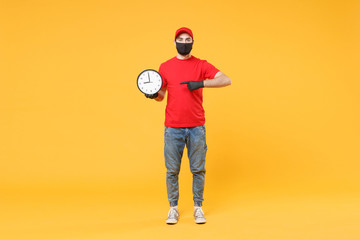 Delivery man in red cap blank t-shirt uniform sterile face mask gloves isolated on yellow background studio Guy employee working courier hold clock Service pandemic coronavirus virus 2019-ncov concept