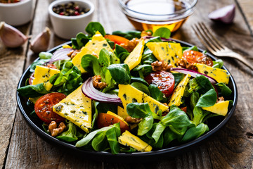 Fresh salad - blue cheese, cherry tomatoes, vegetables and walnuts on wooden background