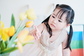 Obraz na płótnie Canvas cute asian little girl playing with tulip flowers with interest having fun feeling happy and enjoying play time, staying at home exploring making using imagination, learning doing practical activities