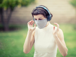 Young girl in a face mask and headphones walking in the park. The new recommendation - everyone to wear masks in public during the coronavirus covid-19 pandemic.