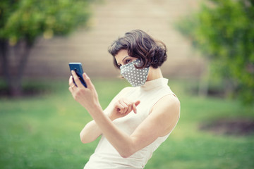 A white woman in a fabric face mask while using her phone for selfie and video chats. The new recommendation -everyone to wear masks in public during the coronavirus pandemic.