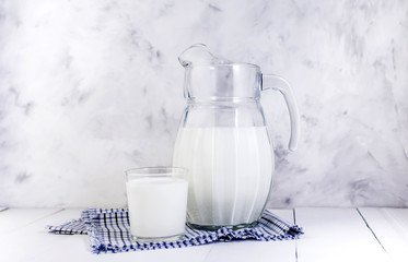 A jug of milk and a glass of milk on a light wooden table on a gray background. Concept of healthy natural products.