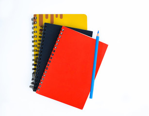 Light blue pencil placed on top of three different colored covered diaries