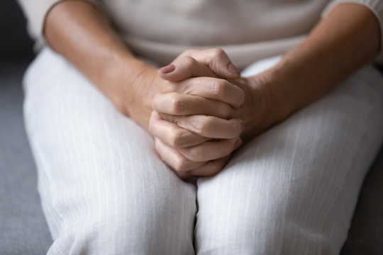 Close up focus on wrinkled female hands clasped together on lap. Stressed older mature woman suffering from loneliness, waiting for health test results, worrying about hard decision alone at home.