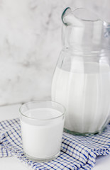 A jug of milk and a glass of milk on a light wooden table on a gray background. Concept of healthy...