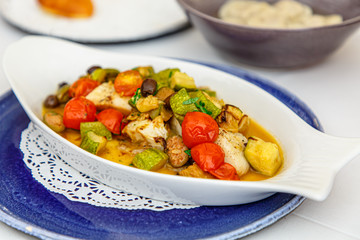 Stewed vegetables (zucchini, potatoes, tomatoes, cabbage) lie on a white plate in the shape of a fish.