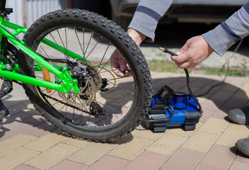 man spins a nipple on the wheel of a children's bicycle, after pumping a flat tire with a compressor. Home maintenance of bike. close-up