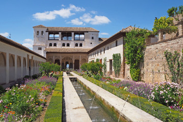 The courtyard of the medieval palace with  green trees, plants, flowers, fountains, old stone walls on the sunny summer day. 