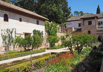 The courtyard of the medieval palace with  green trees, plants, flowers, fountains, old stone walls on the sunny summer day. 