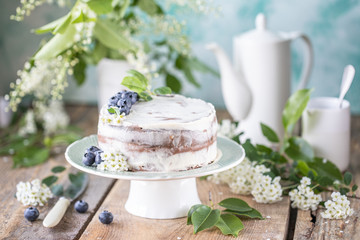 Homemade cherry cake with cream mascarpone on a light background and a bouquet of cherry flowers and lilacs.