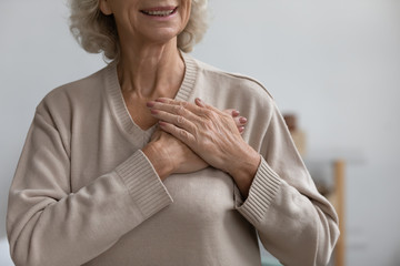 Close up middle aged happy woman thanking God with folded hands on heart, Grateful sincere smiling...