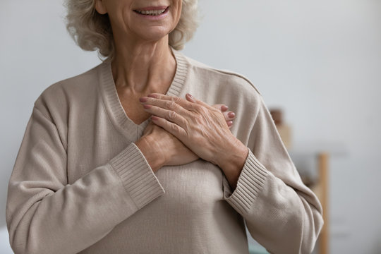 Close Up Middle Aged Happy Woman Thanking God With Folded Hands On Heart, Grateful Sincere Smiling Senior Older Grandmother Holding Hands On Chest Feeling Excited By Good News, Believe Faith Concept.