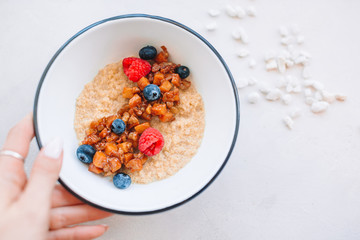 Oatmeal porridge in bowl topped with fresh blueberries, cranberries and homemade crunchy granola