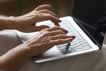 Close up focus on wrinkled female hands typing message on laptop keyboard. Middle aged older woman working on architect building project, sharing pictures chatting communicating in social network.