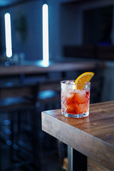 Negroni with a slice of orange on wooden table in a bar, cold colours, cold light, modern bar