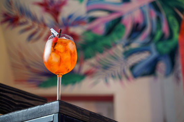 Aperol spritz cocktail with ice and orange on tropical background in a bar