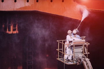worker washing and cleaning in cargo hold of cargo ship in Shipyard on the cherry picker by high pressure water jet gun wearing safety harness for safety concept.