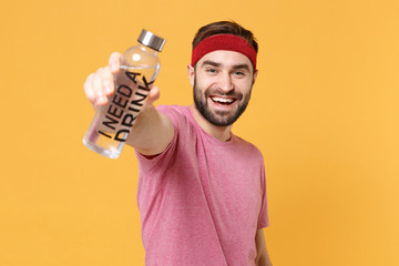 Cheerful young bearded fitness sporty guy 20s sportsman in headband t-shirt spend weekend in home gym isolated on yellow wall background. Workout sport motivation lifestyle concept. Hold water bottle.