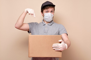delivery man in medical mask holding cardbox pointing on it