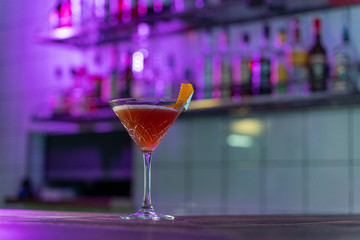 Cosmopolitan cocktail on wooden table in a pink neon light of a loft bar