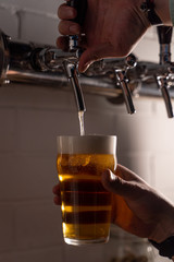 Man pouring light gold beer in a glass from a beer tap, pour with white beer foam, close up hands