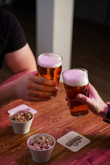 Men are clinking glasses with light beer over a table with beer snacks, in a pub with neon lights