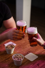 Men are clinking glasses with light beer over a table with beer snacks, in a pub with neon lights
