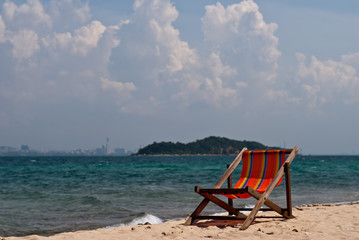 Wooden deck chair with bright fabric on the sandy shore